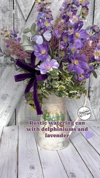 Delphiniums and lavender steal the show in this charming floral arrangement set in a rustic watering can! 
#farmhousearrangements #springdecorationideas #purplehomedecor #wateringcanarrangements 