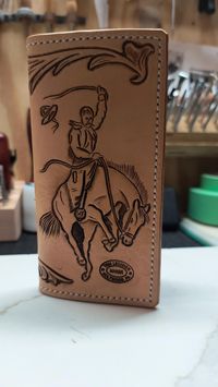 Handmade Hand Tooled leather Roper wallet. Wallet measures 7 inches long and 3.5 inches wide. Hand tooled bucking horse and cowboy on front and floral tooling on rear with letters USA. Wallet body is made from 5-6 0z live oak tooling leather. Interior is made from brown and black mission pig skin. Saddle stitched together by hand with white wax thread. Wallet features 6 card slots, 2 large cash flaps and another flap for cash or whatever. Also holds a checkbook.