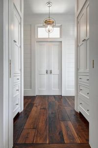 Beautiful natural tung oiled solid walnut plank floors illuminated by a polished nickel Urban Electric Dover bell light white walls lined with inset, built-in white shaker cabinets fitted with polished nickel knobs lead to white hide away doors positioned under a small transom window flanked by white board and batten trimmed shiplap walls.