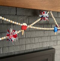 Add the perfect pop of red, white and blue to your decor with a fun beaded garland. Perfect for everything from a photo backdrop at your Independence Day BBQ, to mantel decor, and more!  Garland is available in two designs, one with glittery patriotic mini popsicles, and the other with sparkly firecracker pom-poms; all garlands are approximately 6 feet long with loops on each end for hanging. Each garland has just enough play to allow for swagging, like seen in photos. Each garland is sold separately.  WOOD BEAD + GLITTERY MINI POPSICLE GARLAND Wood beads are approx. 16mm., unfinished and white painted wood.  Glittery popsicles are approx. 3" tall x 1.5" wide.  Garland includes two (2) of each popsicle designs, 6 total.  Garland is strung on white cord.  WOOD  BEAD + SPARKLY FIRECRACKERS W