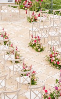 Romantic wedding ceremony setup with white chairs and vibrant floral arrangements lining the aisle. The groups of pink, red, and blush flowers create a whimsical, garden-like pathway, adding a touch of elegance and beauty to the event.