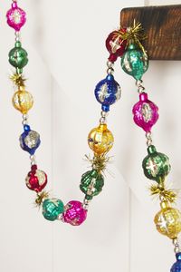 Bring Christmas cheer to your home with this festive garland, adorned with vintage-inspired painted glass spheres and shimmers of tinsel, creating a magical holiday atmosphere.