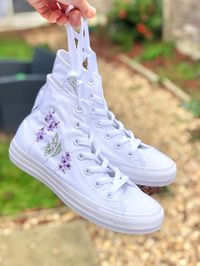 These white monotone Converse trainers are embroidered by hand with my purple floral design.  I offer the option to chose how much embroidery you would like on these particular shoes which vary in price.  - The 'logo embroidery' option is for the leafy design that surrounds the logo on the inside of each shoe.  - The 'outside embroidery' option is for the purple flowers and green foliage which is embroidered on the outside of each shoe.  - The 'all over embroidery' option is for the logo embroidery, outside embroidery, and the date which is embroidered on the back of each shoe if you'd like to make these into bridal or special occasion shoes.  The embroidery is all done in high quality cotton thread to create a completely unique pair of Converse shoes.   I only purchase 100% genuine shoes