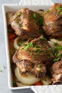 Close up image of white oven proof dish with a layer of cooked vegetables and oven baked turkey thighs set on top