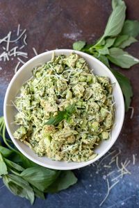 pesto chicken salad in white bowl surrounded by fresh basil