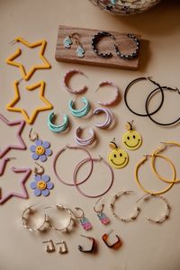 A curated collection of colorful earrings. Bright, bold, statement earrings. Smiley face, good vibes, rainbow, iconic, large, statement accessories, aesthetic jewelry