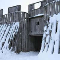 An aesthetic photograph of a fortress entrance made of wood in the tundra. It is covered in snow.