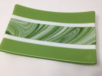 Beautiful art glass in swirling shades of green and white was used in the center of this fused glass tray, bordered by white and light green art glass.  This unique art glass dish will look beautiful on your table, whether used as an appetizer or dessert tray, or on a dresser or night stand to hold keys, jewelry or candles. It's food safe, but not recommended for use in a microwave. Hand washing is recommended to protect the finish. This tray measures 9 3/4" by 6 and rises 1 1/4" at the corners.