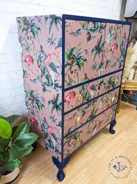 The frame, inner cupboard and cabriole legs have been hand-painted in a beautiful, deep blue navy colour. The body and drawer fronts have been decoupaged in a luxury Muck N Brass wallpaper, ChiMiricle Pink, which features a mythical, botanical garden design. The drawer edges have been painted with a dark and bold pink colour. The body, drawer fronts and legs have been coated with varnish to protect the finish and make it more durable. Gold drawer handles featuring parrots, leopards and monkeys h