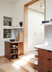 The finishes in the apartment were inspired by mid-century material palettes, with warm wood, creamy white walls, and earth tones. The couple have an extensive collection of souvenirs from traveling, so open display shelving was featured in the design. The custom kitchen cabinetry is walnut with a natural oil finish, which is a nice counterpoint to the warm Douglas-fir flooring. The stone countertops are a variety of marble called Fior Di Bosco, which has warm veins throughout.