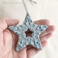 This little star is made from white earthenware clay, imprinted with pattern and finished in a bright, glossy glaze. It has been fired in an electric kiln twice, once to the bisque stage and then a second firing for the glaze. It measures 8cm wide x 7.5cm height x 1cm thick. It can be hung outside.   Copyright Dottery Pottery 2008-2022. This design has been registered and may not be reproduced.