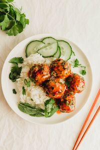 A white plate of rice and Thai pork meatballs glazed with chili sauce.