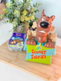 Scooby-Doo’s™ favoriete snack is geen mysterie. Trakteer jezelf op de Scooby™ with Scooby Snacks™ – Scentsy Warmer, bestaande uit de iconische snackdoos met een schattige verstekeling. Scooby’s™ beste vriend Shaggy™ maakt zelfs zijn opwachting in de warmerschaal!  Afwerking: Handgeschilderd  Vermogen: Element  Afmetingen: 21 cm hoog  Materiaal: Keramiek