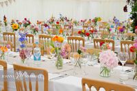 Multi coloured flowers in jars scattered along wedding tables. Summer wedding.