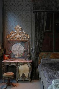 You must see to believe the beauty of this antique vanity table that serves as a nightstand in this classically designed master bedroom by Andrea Michaelson. From the ornately painted wood in shades of cream and soft green to its rose marble top, the piece makes a magnificent statement. The designer placed an antique French painting and ornate gold wall sculpture above the vanity to heighten its effect in the room.