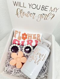 Present your flower girl with a delightful proposal box that will surely make her smile. Inside, she'll discover a charmingly colorful flower girl t-shirt, adorned with whimsical designs to celebrate her special role. Accompanying this are adorable flower daisy sunglasses, perfect for adding a touch of playful flair to her ensemble. To make her feel even more special, include a personalized sippy cup or mini tumbler in her favorite color, ensuring she can stay refreshed in style throughout the c