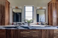 modern primary bathroom, double sinks, mirrors, bathroom lighting, black and white natural stone counter tops, stained wood cabinets, brass pulls, bathroom storage