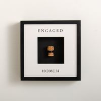 A lovely way to save the memory of the first toast to the newly engaged couple. When the frame is received, the cork from the special occasion is tied easily with a discreet black ribbon and displayed in a deep frame. A special keepsake of the first champagne or prosecco the couple popped once they were engaged or married. Choose either a superb high quality finished black or a white frame. The design will read 'ENGAGED' at the top of the frame (unless you ask for something different) and it all