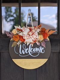 Welcome fall with this handcrafted "Welcome" door hanger. It's crafted with love, featuring fall florals, a rustic bow, and durable wood.  Whether you are into farmhouse or modern decor, this piece is a perfect fit.   It's a sweet way to welcome guests or a thoughtful seasonal gift for someone special.  Pick your size and let the fall fun begin at your front door! *ABOUT THIS DOOR HANGER Greenery/Bow are included and secured with staples Hand cut rounds from 1/2" birch plywood Round Size Options: 15", 18", 20" and 22" Comes with jute rope attached to hang sign Words are permanent outdoor vinyl Back is unfinished Wood is sealed so that it is suitable for outdoor use *Each door hanger is stained and made to order, so you can expect some slight variations may occur. To ensure durability, ever