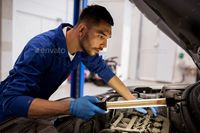 mechanic man with lamp repairing car at workshop by dolgachov. car service, repair, maintenance and people concept ¨C auto mechanic man with lamp working at workshop#car, #workshop, #dolgachov, #repairing