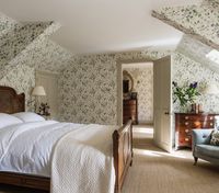 Bedroom interiors by Sutton House Interiors. Wardrobes used to run along the entire wall where the bed is now placed. The middle two cupboards were removed to create more space, and so the bed could be placed facing out towards the windows.  The wallpaper is Sweat Pea by Cole & Son, its small unstructured design drawing your eye away from the large structural beams. The wallpaper runs through into the dressing room to create a cohesive transition within this suite of rooms.