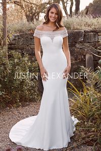 This crepe fit and flare wedding gown is for the refined bride that likes vintage appeal. With a beaded off the shoulder neckline that stands out against the simplicity of the gown. Pearl buttons extend to the end of the chapel length train.