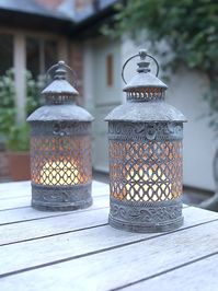 Attractive grey metal lantern with intricate fretwork pattern creating cosy evening candlelight around the home and garden. Perfect for pillar candles for long lasting lighting. Each lantern has a glass surround set within a metal frame with top vent and handle. Distressed metal finish gives a lovely vintage feel. made from: Metal dimensions: Diameter 16cm x Height 36cm