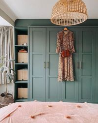 a cozy bedroom with green IKEA Pax wardrobes, with gold handles and open shelves, a bed with pink bedding, a pendant lamp