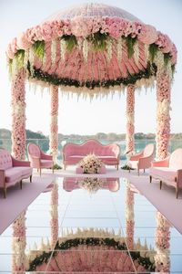 The image showcases a breathtaking modern Indian wedding mandap, adorned with a stunning floral dome and mirrored floor.