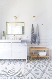 Beautifully designed gray and white bathroom features an Urban Outfitters Plum & Bow Connected Stripe Rag Rug placed on Cement Tile Shop Tulum II Tiles in front of an Ikea Hemnes/Odensvik Washstand adorning CB2 Marble White Disc Drawer Pulls and a brass faucet by Delta.