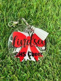 Cheer Keychain / Bag Tag IF YOU NEED YOUR ORDER BY A CERTAIN DATE, PLEASE MESSAGE US FIRST TO ENSURE WE CAN DO IT IN TIME This item is a 3-inch acrylic keychain, which also could be used as a bag tag or zipper pull. Each keychain has a pom pom on the back side, and a bow with name on the front. A short team name can be added also. (See picture) Also included with each is a cheer charm and white tassel. Name, bows, and pom poms are permanent adhesive vinyl. Each has a standard keychain along with