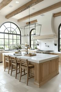 french farmhouse style kitchen with cream walls, wood cabinets and woven barstools with large arched window