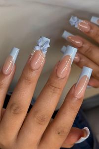 Elegant and poised, these long coffin nails feature a classy French tip in a soothing pastel blue. The highlight is a beautifully crafted 3D bow embellishment on the accent nail, complemented by a delicate string of pearls at the base, exuding a sense of sophisticated charm. A perfect blend of subtlety and eye-catching detail for a refined prom look. ✨  // Photo Credit: Instagram @nailsbyoddica