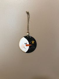 This Wooden Round "Snowman" Ornament was hand painted by me on a round cut out piece of wood.  I made and sold several a while back that were cut from a tree branch that was in my yard and they turned out cute, so I decided to make some more. These are a little different and painted on regular pre-cut wood. The background is black and the snoman white.  I also spattered the background.  It hangs from a jute cord with two craft beads. It has a gold star with some glitter paint and has been sealed with a clear satin spray of mod podge.  Measurements are approximately 3.25" x 3.25".