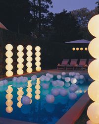 Geometric "topiaries" inspired by the paper sculptures of Isamu Noguchi stand on both sides of this swimming pool. A few white plastic beach balls tied to weighted lines float in the pool like pearls cut loose from a giant strand (for safety, never cover the surface of a pool with a large number of balls).