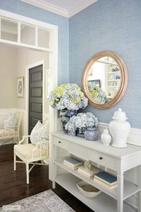 A beautiful and classic white console table display for summer with blue and white ginger jars and vases, arranged with gorgeous blue and green hydrangeas. Stunning Brass and gold hardware accents and gorgeous blue grasscloth in the entryway bring an elegant and sophisticated feel.