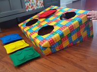 Lego birthday party, DIY bean bag toss made with black beans, felt and a hot glue gun. Board is made with a diaper box covered in wrapping paper