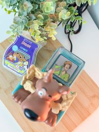 Scooby-Doo’s™ favoriete snack is geen mysterie. Trakteer jezelf op de Scooby™ with Scooby Snacks™ – Scentsy Warmer, bestaande uit de iconische snackdoos met een schattige verstekeling. Scooby’s™ beste vriend Shaggy™ maakt zelfs zijn opwachting in de warmerschaal!  Afwerking: Handgeschilderd  Vermogen: Element  Afmetingen: 21 cm hoog  Materiaal: Keramiek