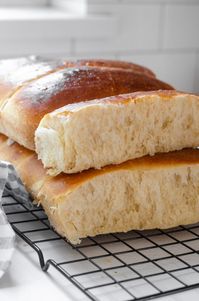 A stack of homemade sourdough hotdog buns on a black wire cooling rack with a linen napkin off to the side.