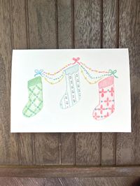 "The stockings were hung by the chimney with care, in hopes that St. Nicholas soon would be there!"  These colorful, festive stockings were painted by hand using 100% non-toxic watercolor paints. This folded card is 5x7 inches and comes with a white envelope. Blank on the inside for you to write your own festive holiday message!