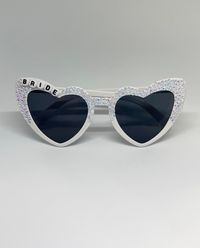 These personalized sunglasses are for adults and are the perfect combo of sparkly and classy. These sunglasses can be customized whether you want "Bride", "Bridesmaid", "Mrs. XYZ", "Bride Tribe", "Squad", etc.  DETAILS- * Choose your color frame (pink or white) * Choose if you'd like half or full rhinestones (photos above are half) * Choose your slogan! You can personalize with your name, bridal name, anything you'd like! White frames come with clear rhinestones & Pink frames come with light pin