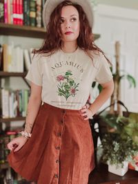 This is the Unisex-Style Vintage February Aquarius Birth Flower Kitten Tee. It is a cottagecore styled heavy cotton tee with vintage botanical illustrations salvaged from old ephemera. January's birth flowers are snowdrops and carnations, and three common traits of aquarius are that they are innovative, progressive, and revolutionary! This classic T is made with cotton, sometimes polyester (depending on the color) and has no uncomfortable side seams. This design is an original, created by Jillia