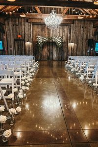 White roses and greenery adorn the arbor and white roses in bud vases decorate the aisle.