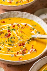 This delicious, healthy butternut squash soup recipe features a rich & creamy blend of roasted squash, garlic, chicken broth, & coconut milk. Topped with crispy chopped bacon and cilantro pumpkin seeds, this beautiful soup bursts with flavor in every bite. Paleo, Gluten-Free, Dairy Free, and Whole30. #butternutsquashsoup #souprecipes #dairyfree #paleo #soup #vitamixrecipes