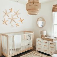 Neutral beach themed nursery with wood crib, white dresser, round mirror, woven lamp, and vintage rug. See this and 10 more inspiring ocean & beach themed nurseries at thestyledabode.com.   Nursery - nursery ideas - nursery room inspiration - nursery decor - nursery themes - ocean themed nursery - ocean nursery theme - ocean nursery decor - ocean nursery girl - ocean nursery boy - ocean nursery ideas - beach themed nursery - beach themed nursery neutral beach themed nursery ideas.