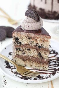 This Oreo Cookies and Cream Layer Cake is layers of moist vanilla cake loaded with crushed Oreos. The cake is filled with a chocolate fudge filling and topped with an easy Oreo buttercream. Glazed with chocolate ganache, this Oreo cake recipe is a showstopper! #oreocake #cookiesandcream #oreo #layercake #homemadecake #cake #oreolayercake #cookiesandcreamcake #cookiesandcreamfrosting #oreofrosting