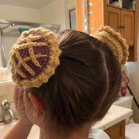 "My daughter is obsessed with pie and I've been messing around with crochet for the past year so this creation was inevitable. The pie is built off of an elastic hair tie at its base, which allows for you to stretch it open to fit over a sturdy bun of hair (refer to video).  There are 2 colors/flavors so far, Orange/Pumpkin and Maroon/Raspberry. Made with medium 7oz 100% Acrylic Yarn and clasp free thick elastic hair tie.  Each pie measures: 3.5\" x 3.5\" x 2\" outside measurement (not stretched sample had 1.5\" inside depth pictured) Delicate Care Directions state: Hand wash, lay flat to dry. Care directions of yarn says : Machine wash warm, gentle cycle. Tumble dry low. Do not over dry (though I will assume that's for if you make it into a blanket or something else hefty, not intricate p