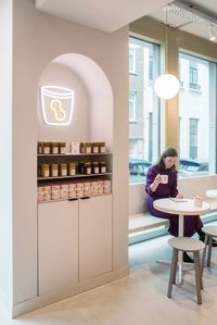 The other half of the space, nearest to the window, houses low seating areas and is finished in warm, milky-white colours that complement the building's grey facade.