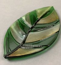 "This kiln-formed leaf tray combines green glass with panels of metallic iridescent glass. The gently sloping leaf tray is perfect for display, catching your keys, or for serving up crackers at your next party. Handmade fused glass tray is kiln fired, fire polished, and properly annealed for strength and durability. Hand washing recommended. Do not use tray in microwave. Tray is available in 2 sizes: Large: 12\" x 7\" Small: 6\" x 4\" As each tray is individually handmade, actual tray may vary s