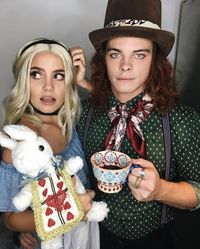 blue-eyed man, dressed like the mad hatter, posing with a woman, dressed like alice, holding a stuffed white rabbit, cute couple halloween costumes